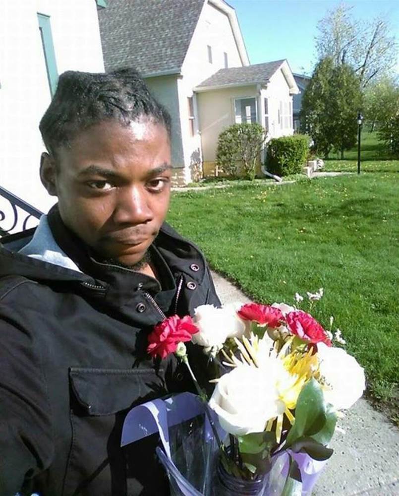 Jamar Clark stands in the sun with a bouquet of flowers.