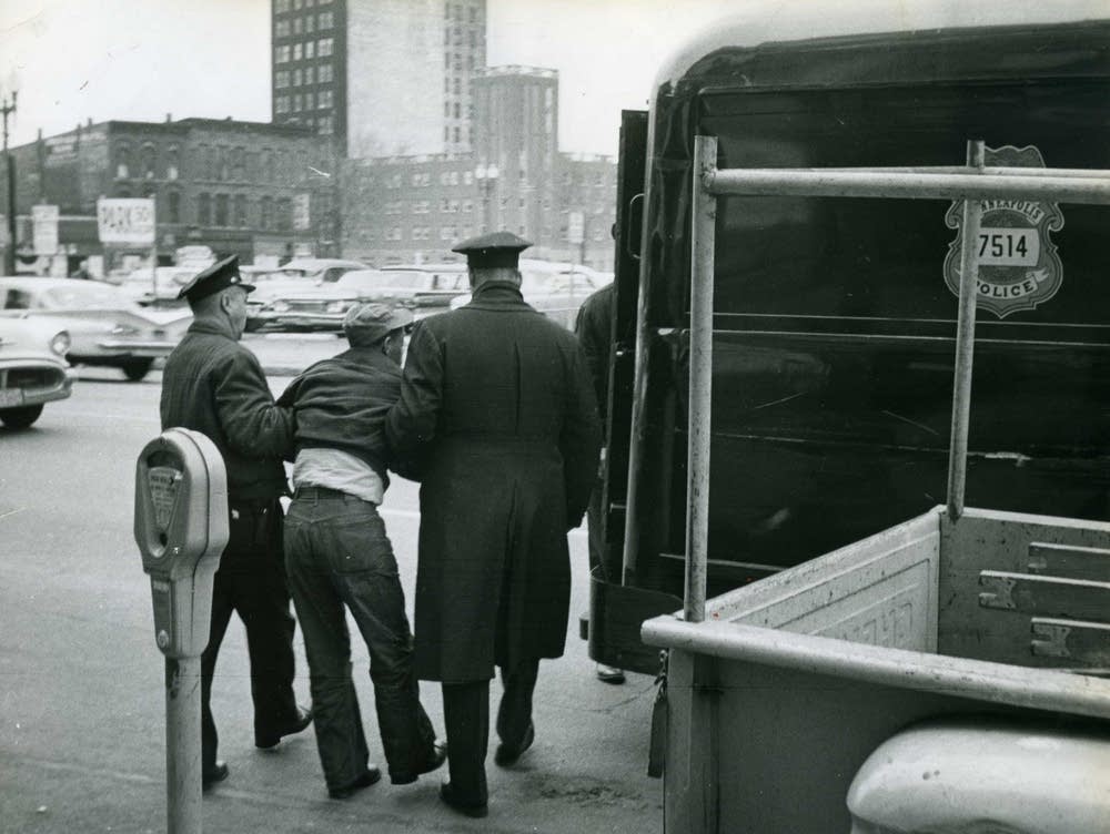 A black and white photo of two police from the back arresting a man.