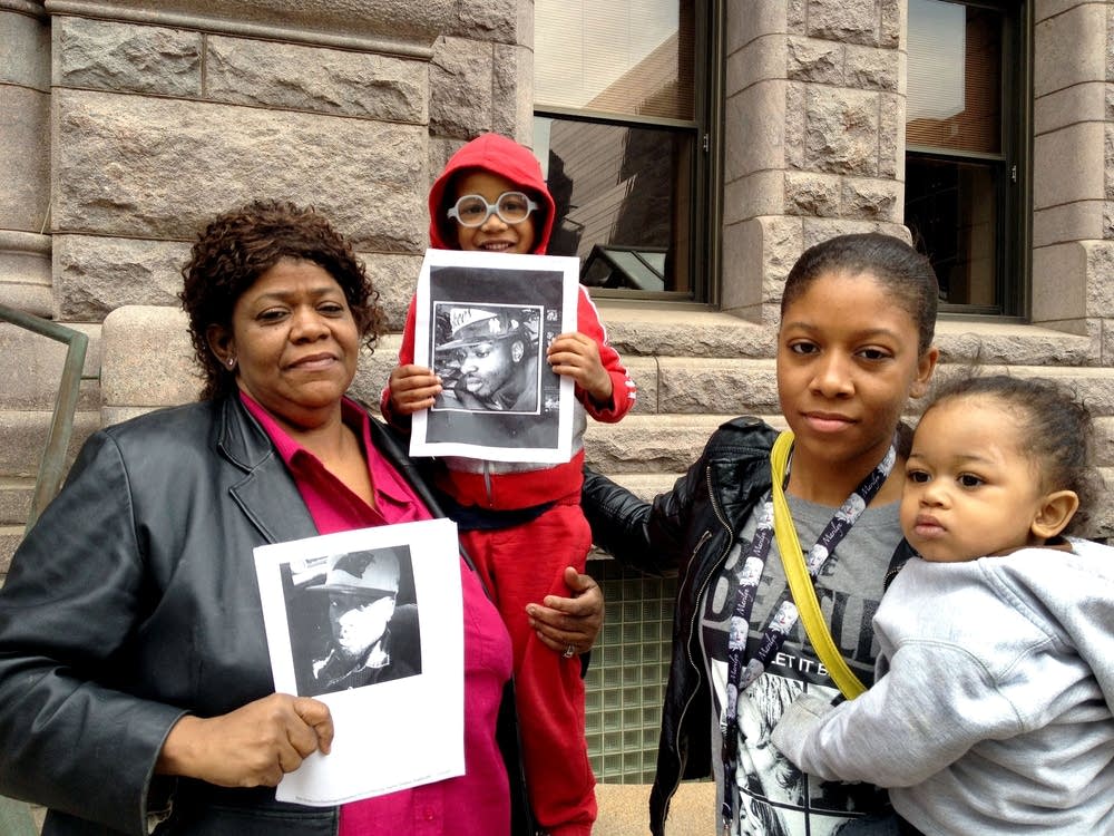 The Family of Terrance Frankling stand in front of a stone building, holding black and white photos of Terrance.